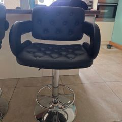 2 black faux leather bar stools with padded seats, armrests and chrome bases.