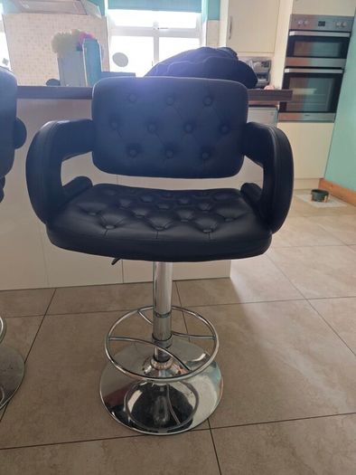 2 black faux leather bar stools with padded seats, armrests and chrome bases.