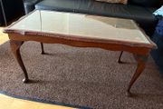 Vintage Queen Anne-style wooden coffee table featuring cabriole legs, a glass top protecting an inset leather surface with gold tooling