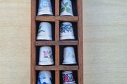 Collectible porcelain thimbles in a wall-mounted wooden display case