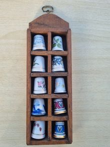 Collectible porcelain thimbles in a wall-mounted wooden display case