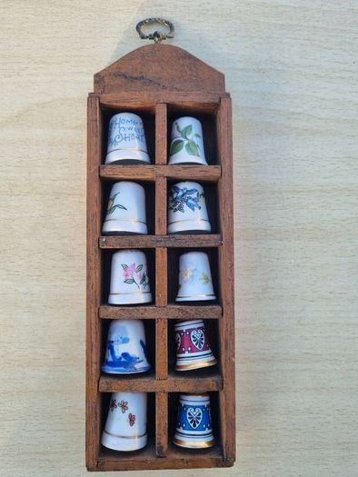 Collectible porcelain thimbles in a wall-mounted wooden display case