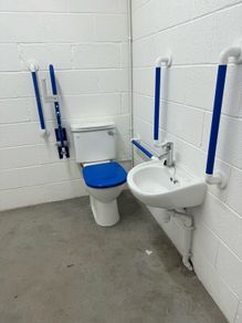 Toilet with handrails, two sinks, unused.