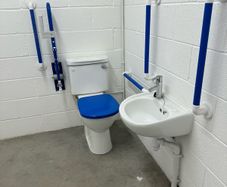 Toilet with handrails, two sinks, unused.
