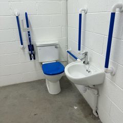 Toilet with handrails, two sinks, unused.