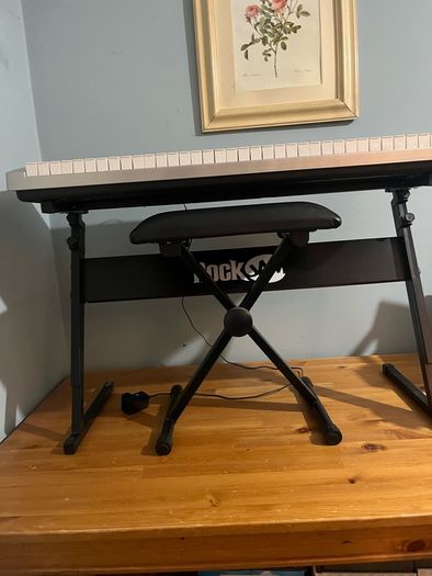 RockJam Electronic Keyboard Piano set up on a sturdy, matching heavy-duty Z-frame stand and an adjustable padded X-frame RockJam Keyboard Bench resting on a wooden surface.