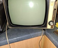 Ideal Prop, Vintage Working Boots Audio TV12 Portable Black and White CRT Television, featuring a cream plastic casing with side control dials and a 12 inch screen. Designed with dual power capabilities supporting standard mains voltage (240V) as well as 