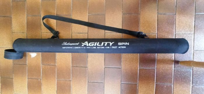 Shakespeare Agility Spin fishing rod. 11 feet (3.30 meters) in length. The item includes a black carrying tube with a strap for transport.