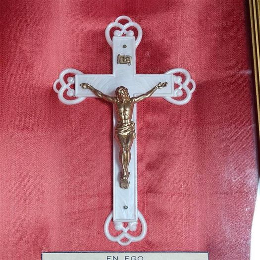 antique framed crucifix featuring a white ornamental cross with a metallic corpus of Jesus Christ mounted over a red  backing inside a gilded wooden frame. Devotional item.