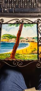 Hand painted tile from Palamos, Playa La Fosca La Fosca beach in Palamos, Costa Brava, Spain. heled in black costirorn holder