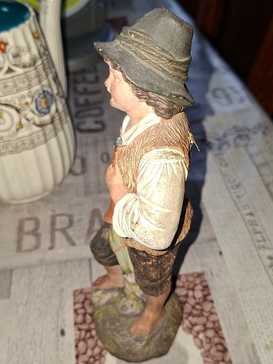 Old Painted Terracotta of a Young Country Boy Holding a Flute, standing on a rocky base. It resembles late 19th- or early 20th-century European decorative sculptures, such as pieces produced by makers like Goldscheider