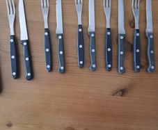 A 12-piece stainless steel steak knife and fork set with wooden riveted handles.