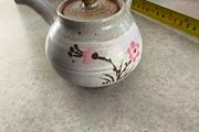 Japanese Side-Handle Teapot Kyusu 300cc  speckled ceramic side-handle teapot (kyusu) features a hand-painted pink cherry blossom (sakura) or plum floral branch motif against a light gray or cream stoneware body