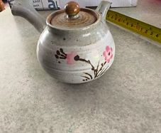 Japanese Side-Handle Teapot Kyusu 300cc  speckled ceramic side-handle teapot (kyusu) features a hand-painted pink cherry blossom (sakura) or plum floral branch motif against a light gray or cream stoneware body