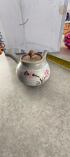 Japanese Side-Handle Teapot Kyusu 300cc  speckled ceramic side-handle teapot (kyusu) features a hand-painted pink cherry blossom (sakura) or plum floral branch motif against a light gray or cream stoneware body
