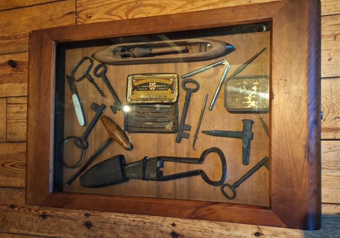 vintage shadow box containing a mix of antique tools, keys, and a loom.