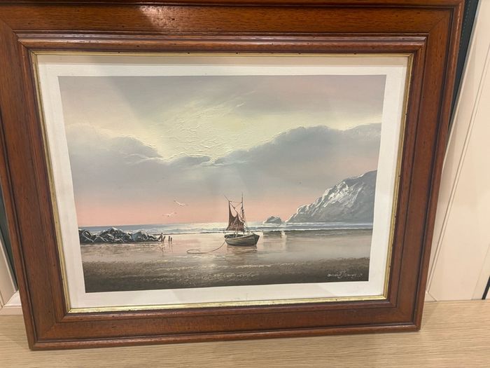 This artwork is a coastal oil painting featuring a traditional single-masted sailing boat stranded or anchored on a calm shoreline, signed by contemporary marine artist David James