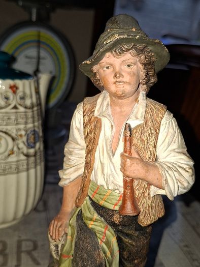 Old Painted Terracotta of a Young Country Boy Holding a Flute, standing on a rocky base. It resembles late 19th- or early 20th-century European decorative sculptures, such as pieces produced by makers like Goldscheider