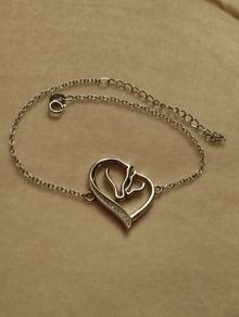 A silver bracelet with a heart-shaped pendant featuring a horse and foal's head.