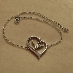 A silver bracelet with a heart-shaped pendant featuring a horse and foal's head.