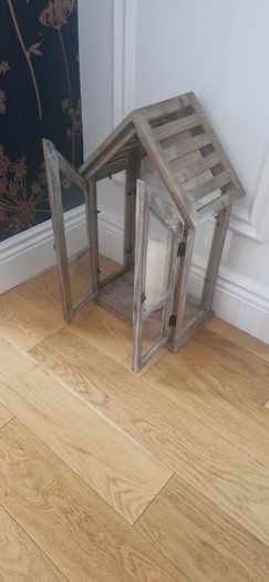 Rustic house-shaped wooden lantern featuring glass panel doors and a pitched roof design