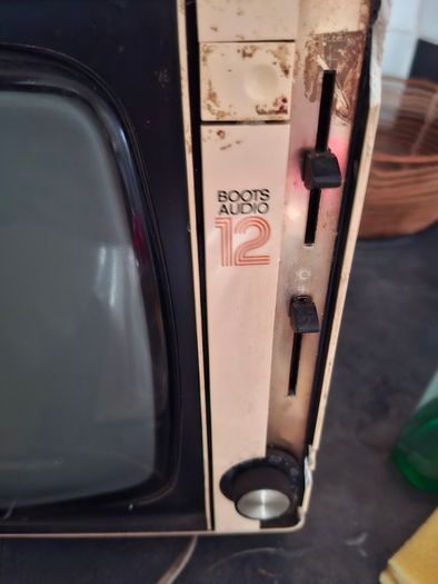 Ideal Prop, Vintage Working Boots Audio TV12 Portable Black and White CRT Television, featuring a cream plastic casing with side control dials and a 12 inch screen. Designed with dual power capabilities supporting standard mains voltage (240V) as well as 