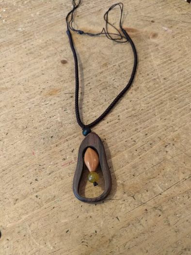 wooden pendant necklace featuring a dark brown wooden frame, a light-colored central bead, and a small dark yellow stone accent on an adjustable braided cord.