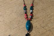 This Bohemian-style necklace features a prominent central blue bead with a leaf-shaped tassel.