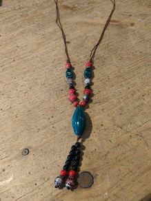 This Bohemian-style necklace features a prominent central blue bead with a leaf-shaped tassel.