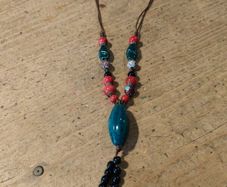 This Bohemian-style necklace features a prominent central blue bead with a leaf-shaped tassel.