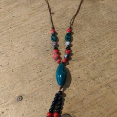 This Bohemian-style necklace features a prominent central blue bead with a leaf-shaped tassel.
