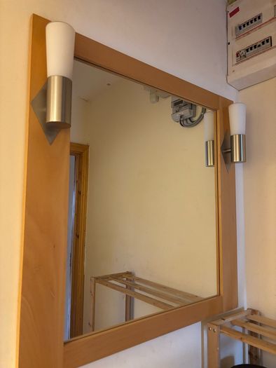 This pine-framed mirror includes two attached wall sconces for lighting.