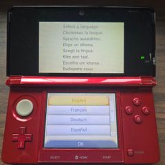 Nintendo 3DS in metallic red, comes with charger and Super Mario Maker for Nintendo 3DS. The console is used and has visible marks/scratches from normal use, mainly on the outside casing and around the edges, but it will be cleaned before posting/collecti