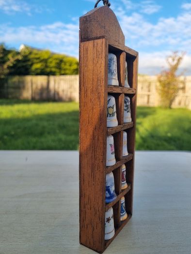 Collectible porcelain thimbles in a wall-mounted wooden display case