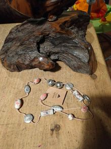 This handmade necklace features a combination of ceramic floral beads and silver-toned metal beads on a pink cord.