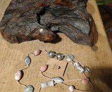 This handmade necklace features a combination of ceramic floral beads and silver-toned metal beads on a pink cord.