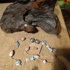 This handmade necklace features a combination of ceramic floral beads and silver-toned metal beads on a pink cord.