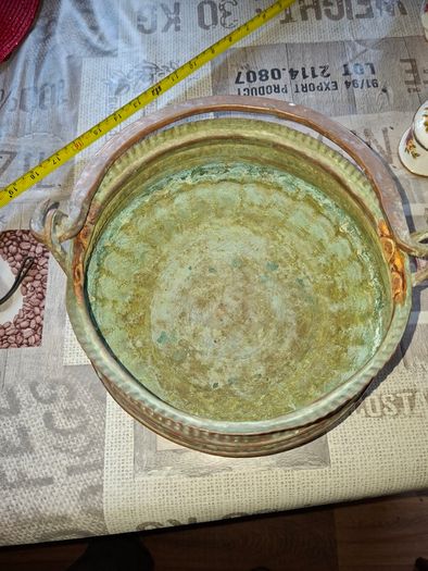 Antique Copper Cauldron features a Rustic Patina, a Swing Handle, and Distinctive Ribbed Detailing around the Rim. It resembles vintage metal pots often used for hearth decoration or as Planters. The piece shows significant oxidation and aging, characteri