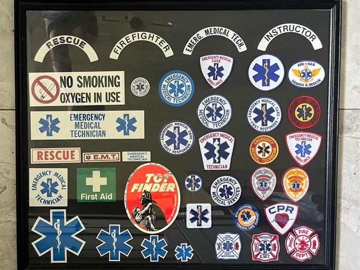 Framed display of EMS (Emergency Medical Services) including Fire and Ambulance Service Patches and stickers. Frame measures 34 incehs X 29 inches