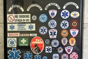 Framed display of EMS (Emergency Medical Services) including Fire and Ambulance Service Patches and stickers. Frame measures 34 incehs X 29 inches