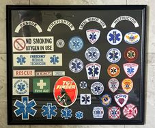 Framed display of EMS (Emergency Medical Services) including Fire and Ambulance Service Patches and stickers. Frame measures 34 incehs X 29 inches