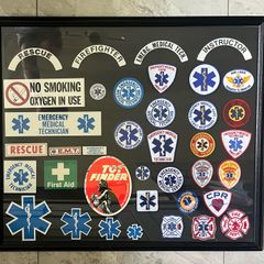 Framed display of EMS (Emergency Medical Services) including Fire and Ambulance Service Patches and stickers. Frame measures 34 incehs X 29 inches