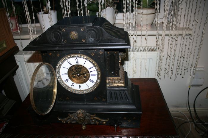 Victorian French Black Slate Mantle Clock (Very large and heavy) with bronze ornamentation Oversized. Open escarpment slate plate Roman numerals. Circa 1890s. Accented with Trojan head. Flanked by two Hellenistic ladies heads on sides. Rose cartouche mask