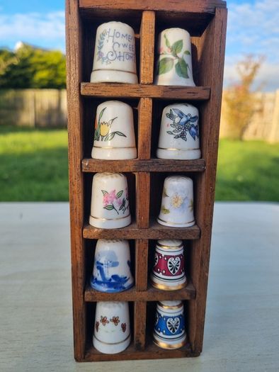 Collectible porcelain thimbles in a wall-mounted wooden display case