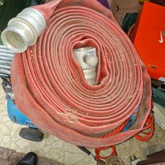 Coiled red canvas fire hose with ribbed aluminium coupling and internal fitting visible at centre, Postage Available