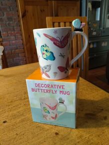 Butterfly Shaped Handle Ceramic Mug, decorated with various colorful butterfly graphics. 3D ceramic butterfly molded directly onto the handle. New in Box.