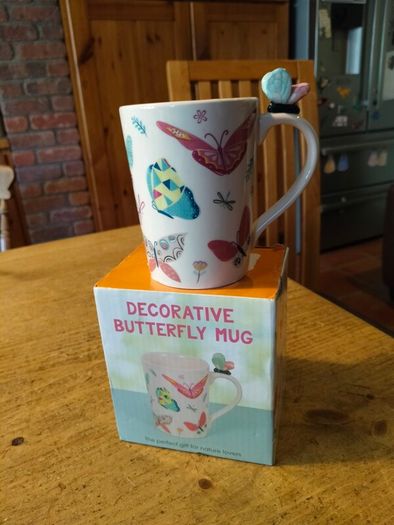 Butterfly Shaped Handle Ceramic Mug, decorated with various colorful butterfly graphics. 3D ceramic butterfly molded directly onto the handle. New in Box.