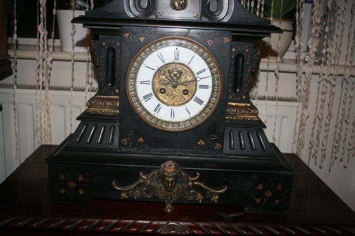 Victorian French Black Slate Mantle Clock (Very large and heavy) with bronze ornamentation Oversized. Open escarpment slate plate Roman numerals. Circa 1890s. Accented with Trojan head. Flanked by two Hellenistic ladies heads on sides. Rose cartouche mask