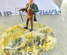 A gentleman holding a walking stick, mounted on what appears to be an onyx or serpentine stone base as ashtray or pine holder.Royal Doulton Figure "Owd Willum . Designed by L Harradine it was issued between 1949 and 1973.