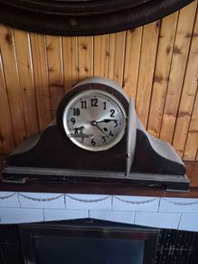 vintage mechanical mantel clock, styled in a traditional "Napoleon hat" or humpback tambour shape with a dark wooden case.